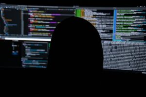Silhouette d’une personne devant plusieurs écrans affichant des lignes de code et des données
